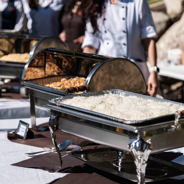 Buffet line with chafing dishes of Thai food, including rice, and a chef in the background.