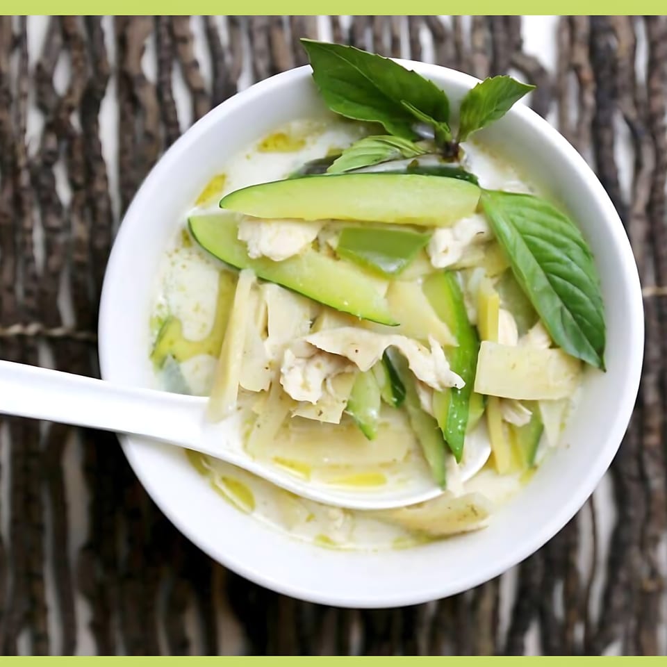 Thai green curry with chicken, bamboo shoots, and zucchini, garnished with basil in a white bowl.