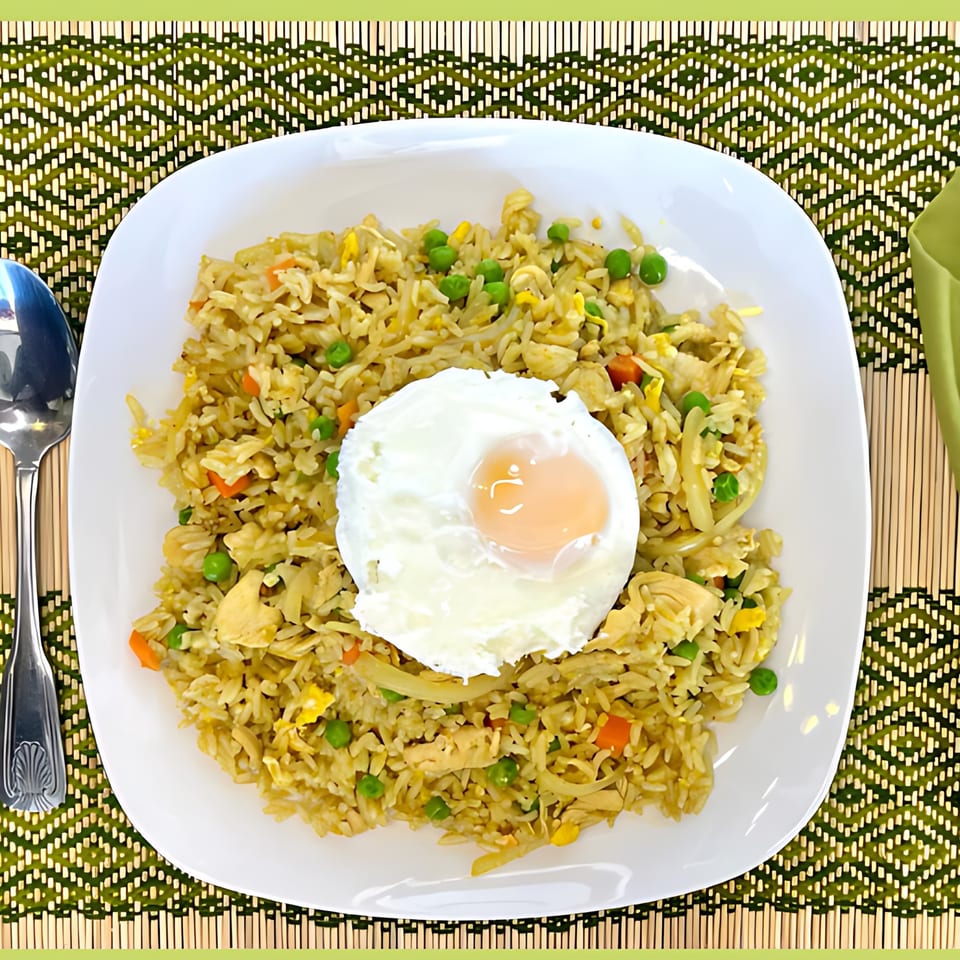 Thai fried rice with chicken, peas, carrots, and a poached egg on a white plate.
