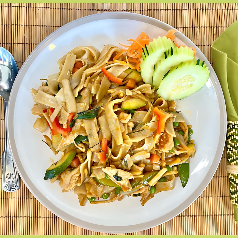Thai Drunken Noodles with chicken, vegetables, and wide rice noodles, garnished with cucumber and carrots.