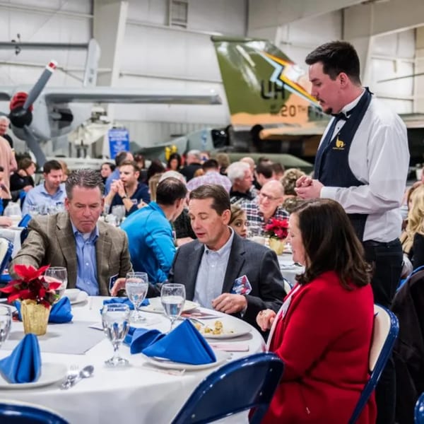 Diners seated at round tables with blue napkins and poinsettias, with airplanes in the background.