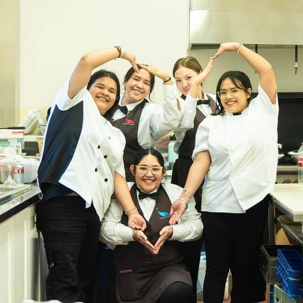Five smiling Bangkok Garden staff members form heart shapes with their hands in a kitchen.
